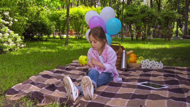 carino bambino mangiare mela e seduto sulla coperta vicino tablet digitale e frutta - Filmati, video
