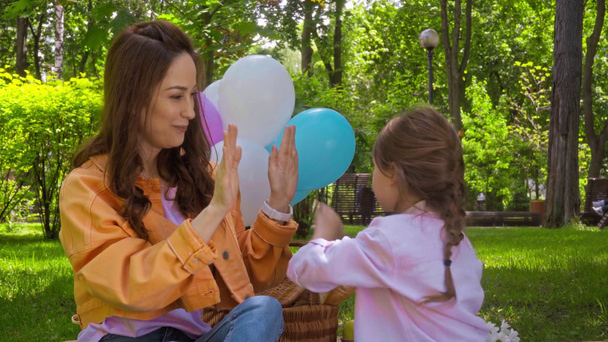 happy mother and daughter playing hand clapping game in park - Filmmaterial, Video