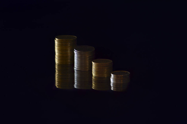 Чотири стопки монет різної висоти на чорному тлі
 - Фото, зображення