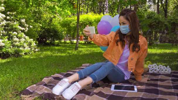 Frau mit medizinischer Maske bei Videoanruf nahe digitalem Tablet im Park  - Filmmaterial, Video