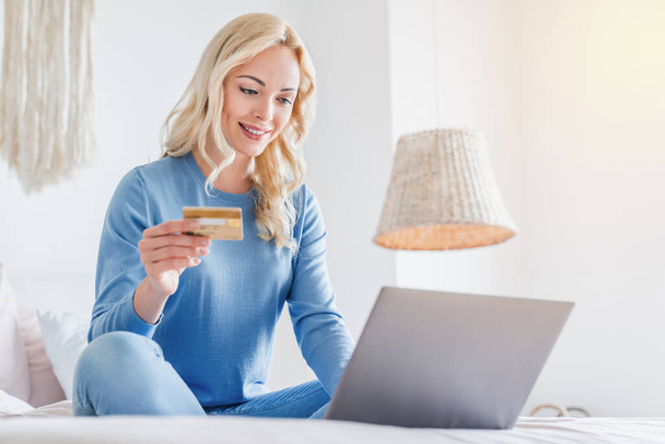 İnternetten alışveriş yapan bir kadın evde yatarken dizüstü bilgisayar ve kredi kartı kullanıyor. - Fotoğraf, Görsel