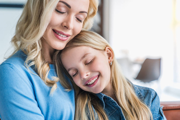 Portrait of happy mother and daughter embracing with eyes closed at home - Foto, Bild