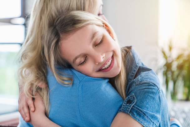 Glückliche Mutter und Tochter umarmen sich zu Hause mit geschlossenen Augen - Foto, Bild