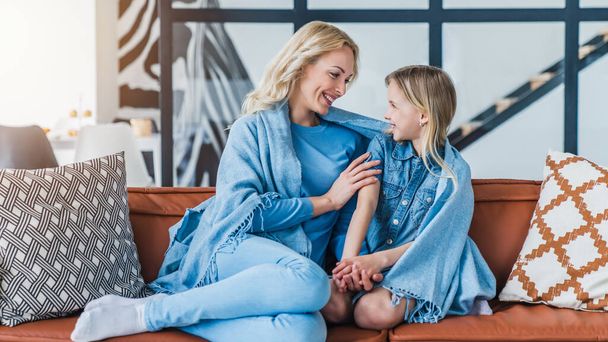 Smiling woman having fun with her daughter while sitting on the couch under blanket - Foto, imagen