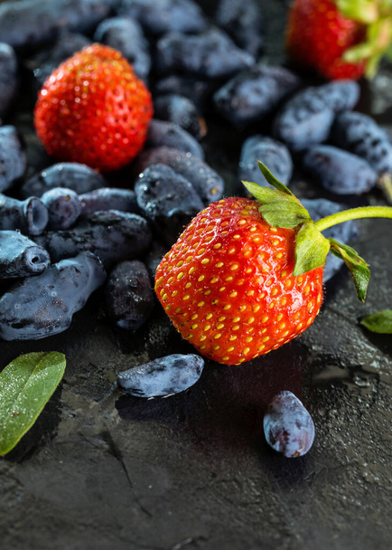 Темные ягоды жимолости и сладкая клубника на тёмном фоне. Понятие здорового и правильного питания
. - Фото, изображение