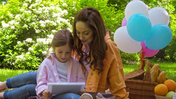 matka wskazując palcem na cyfrowy tablet w pobliżu cute córka w parku - Materiał filmowy, wideo
