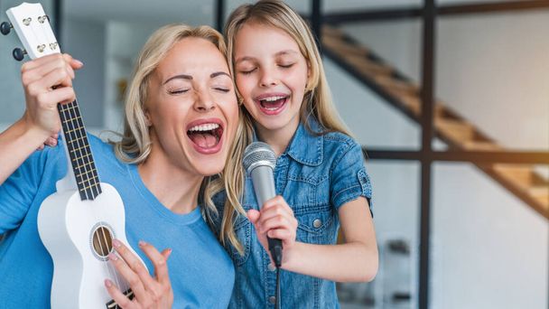 Caucasian mother with little girl singing in karaoke at home - Fotó, kép
