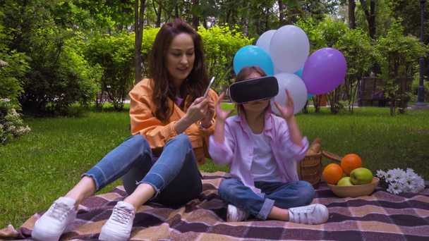 счастливая мать с помощью смартфона рядом с ребенком в наушниках виртуальной реальности
  - Кадры, видео
