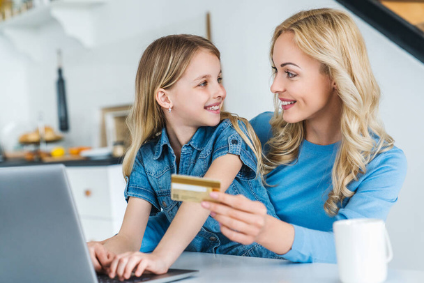 Young caucasian woman online shopping using credit card with her daughter at home - Foto, Imagem