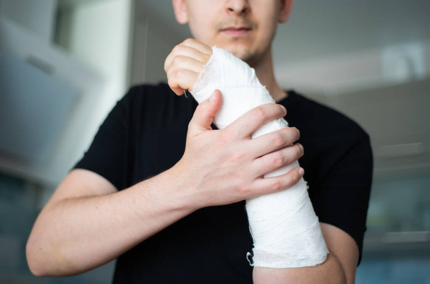 A young man checks the plaster bandage for strength by touching a broken arm close-up - Photo, Image