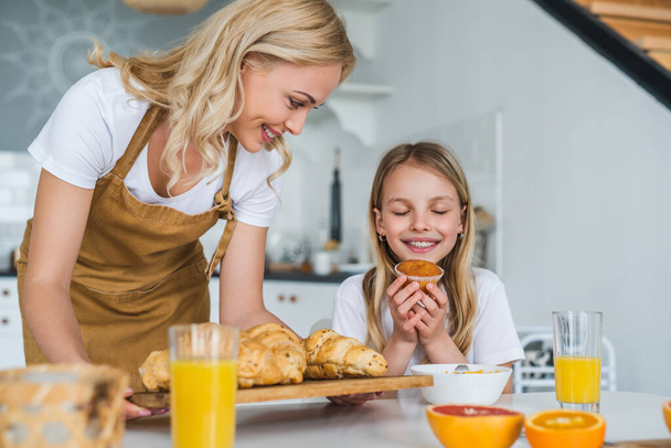 Smiling mother in apron baking cookies for her excited daughter - Fotoğraf, Görsel