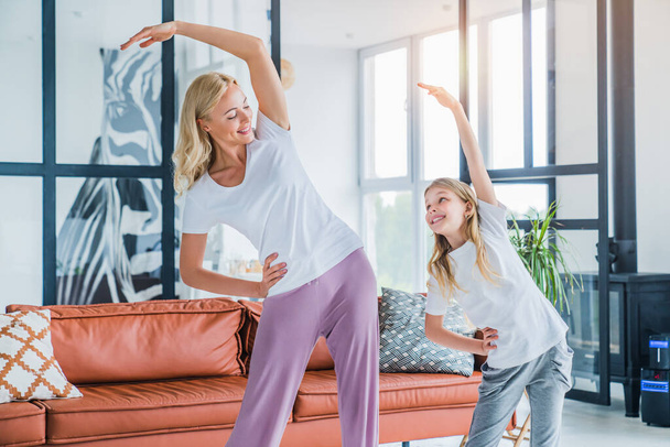 Young adult woman with her kid daughter doing morning fitness exercises at home - Photo, image