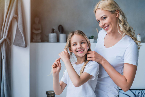 Smailing woman doing hair of her daughter at home - Foto, Bild