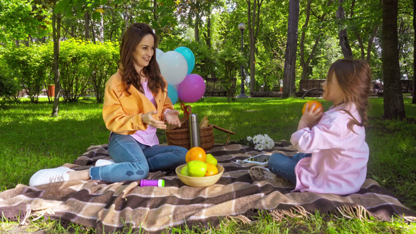 szczęśliwy matka i córka rzucając w powietrzu i złapać pomarańczowy w parku  - Materiał filmowy, wideo
