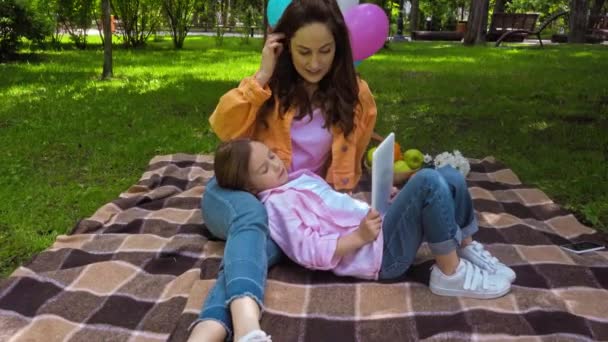 χαρούμενο παιδί ξαπλωμένο κοντά σε ελκυστική μητέρα και χρησιμοποιώντας ψηφιακή ταμπλέτα στο πάρκο - Πλάνα, βίντεο