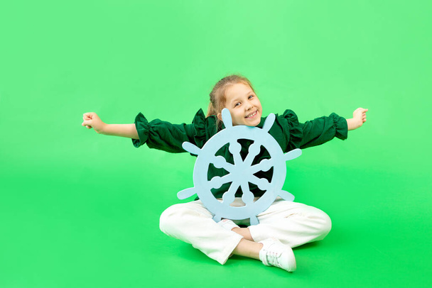 uma menina de 6-7 anos de idade em um fundo isolado verde senta-se com uma âncora, um lugar para texto
 - Foto, Imagem