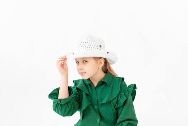 tyttö vihreissä vaatteissa istuu valkoisella taustalla ja pitää hattua, tilaa tekstille - Valokuva, kuva
