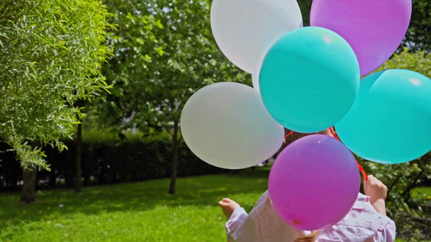 Parkta renkli balonlarla koşan sevimli çocuk.  - Video, Çekim