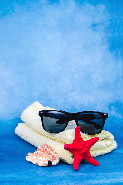 Солнечные очки, полотенце, ракушка и рыба-звезда на синем фоне
 - Фото, изображение
