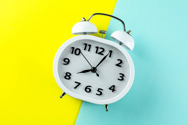 white vintage alarm clock on yellow and blue background. - top view. - Photo, Image