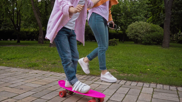 mother holding hands with happy daughter riding penny board  - Footage, Video