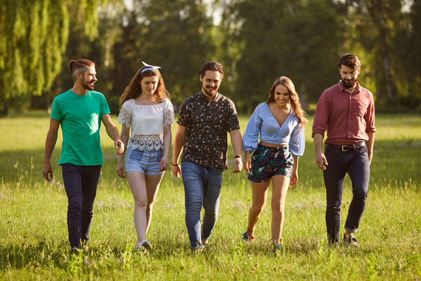 Full length portrait of happy young friends walking in countryside on warm summer day. Group of people on weekend - Foto, afbeelding