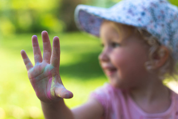 Αξιολάτρευτο κοριτσάκι με ξανθά σγουρά μαλλιά που δείχνει το χέρι της χρωματισμένο από κραγιόνια - Φωτογραφία, εικόνα