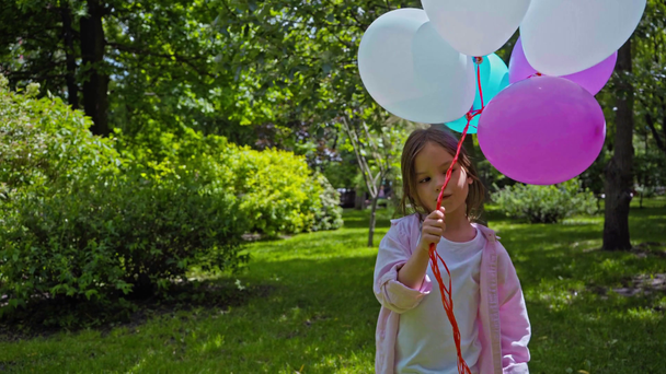 cute kid holding balloons, showing peace sign and sending air kiss in park - Footage, Video