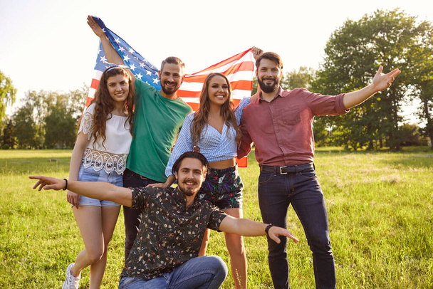 Group of happy friends with American flag in countryside. Young patriotic people with national banner. Independence Day - Zdjęcie, obraz