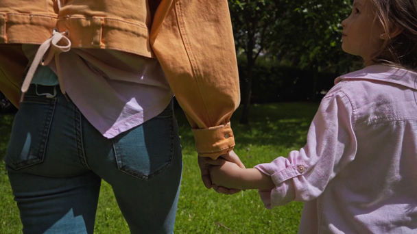 aranyos lány és anya kéz a kézben sétálás közben a parkban  - Felvétel, videó