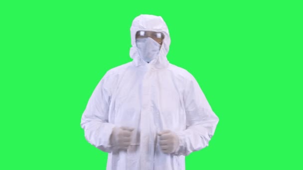 A man in a protective suit with a mask on his head and glasses goes forward on a green background - Video