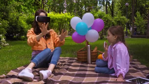 Mutter gestikuliert in Virtual-Reality-Headset nahe Tochter mit Smartphone  - Filmmaterial, Video