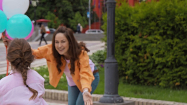 rack εστίαση του παιδιού ιππασία σκούτερ κοντά στη μητέρα με μπαλόνια στο πάρκο  - Πλάνα, βίντεο