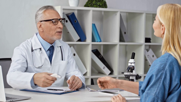 doctor maduro en gafas usando pirómetro en paciente y escribiendo prescripción
 - Metraje, vídeo