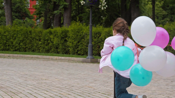 rozkošné dítě na koni kop skútr s barevnými balónky v parku  - Záběry, video