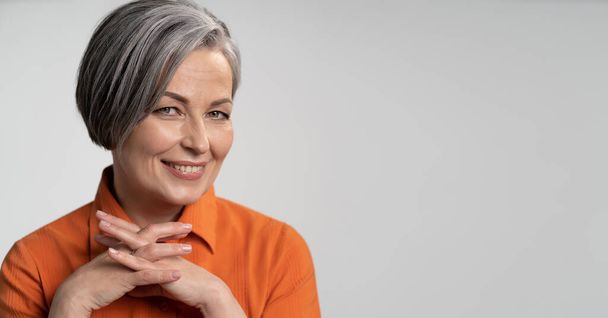 Happy aged woman smiling fingers crossed. Lady with bob hairstyle in orange blouse, head and shoulders portrait. Wisdom concept. Horizontal blank or template with copy spase at right side - Photo, Image