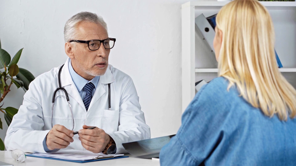 selective focus of mature doctor talking with patient near x-ray  - Πλάνα, βίντεο