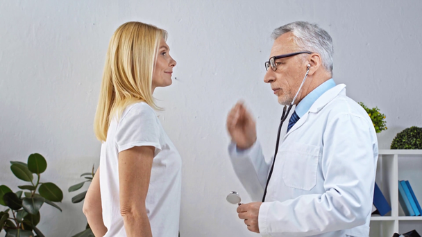 medico maturo esaminando donna e parlando in clinica  - Filmati, video