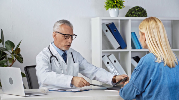 зрелый врач смотрит на рентген и принимает с пациентом в клинике
  - Кадры, видео