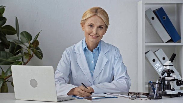 attractive and mature doctor holding pen and using laptop  - Footage, Video