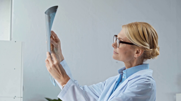 ελκυστική μεσήλικας γιατρός σε γυαλιά κοιτάζοντας ακτινογραφία - Πλάνα, βίντεο