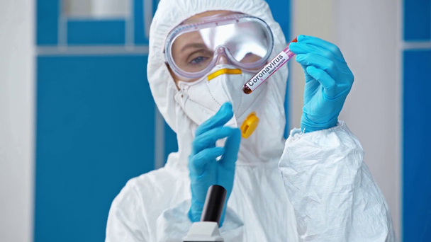 científico en traje de materiales peligrosos mirando el tubo de ensayo con letras de coronavirus
 - Imágenes, Vídeo
