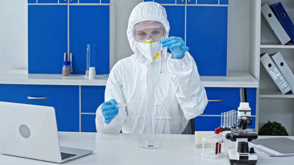 Wissenschaftler fügt Probe im Reagenzglas mit Flüssigkeit nahe Laptop im Labor hinzu - Filmmaterial, Video