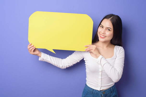 Young woman is holding yellow empty speech on purple background  - Foto, imagen
