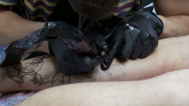 Στενή άποψη ενός επαγγελματία κάνει ένα τατουάζ στο πόδι ενός άνδρα σε ένα σαλόνι. Σχέδιο με περιστροφικό τατουάζ πολυβόλο - Πλάνα, βίντεο