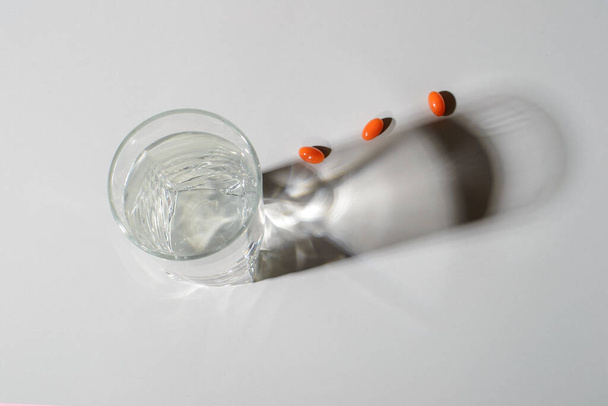 Склянка чистої води з натуральними вітамінами, з тінями на світлому фоні. Вид зверху. охорони здоров'я
 - Фото, зображення