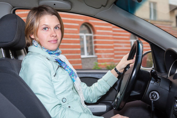 Young woman holding steering wheel of her car, sitting inside on driver place - Foto, Bild