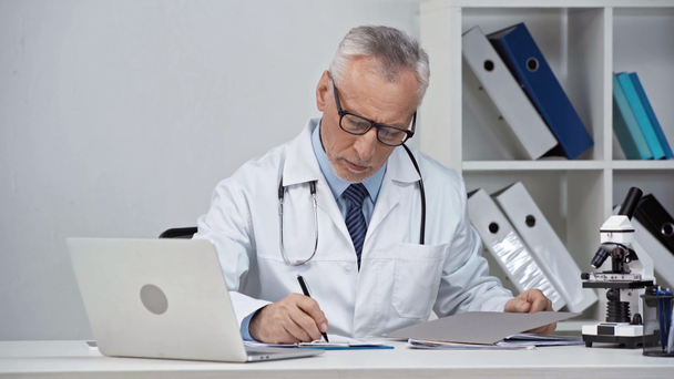 médecin d'âge moyen écrivant la prescription et tenant dossier  - Séquence, vidéo