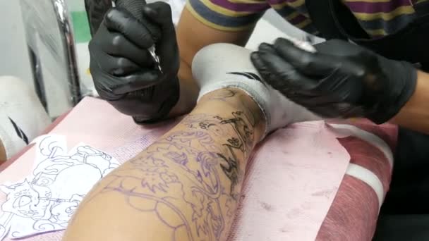 Στενή άποψη ενός επαγγελματία κάνει ένα τατουάζ στο πόδι ενός άνδρα σε ένα σαλόνι. Σχέδιο με περιστροφικό τατουάζ πολυβόλο - Πλάνα, βίντεο