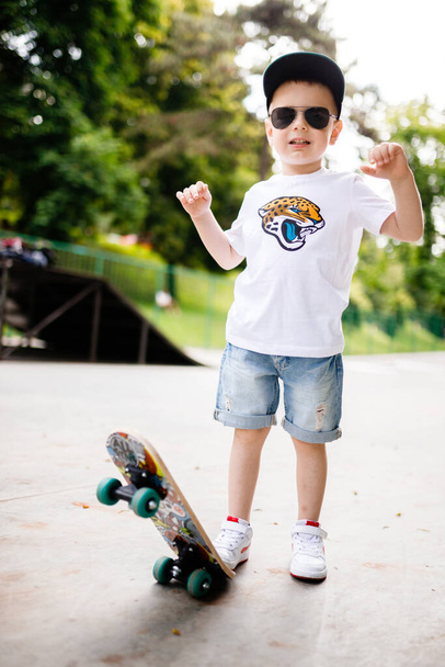 Junge mit Skate in einem Skatepark. Ein Junge mit Brille lernt Schlittschuhlaufen. - Foto, Bild